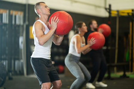 Sportive young guy working out with medicine ball in gym during crossfit workout