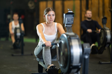 Determined young girl training with rowing machine in sports hall