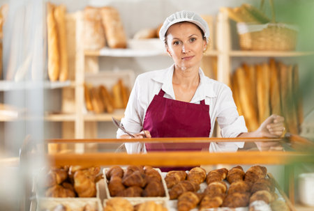 Female baker places fresh croissants on display in shop