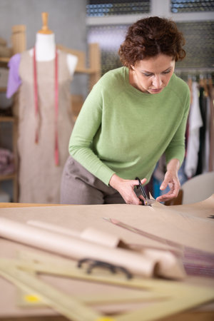 Female fashion maker cutting paper pattern for bespoke garment