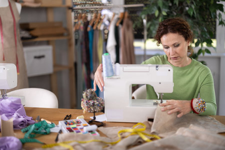 Working in sewing workshop - female dressmaker working at sewing machine making stitches on fabric
