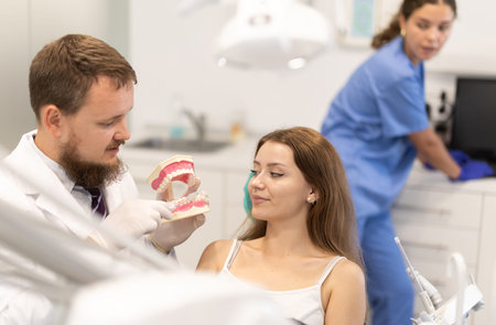 Male dentist shows a jaw model to a young patient in dental clinic