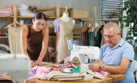 Elderly man sewing female assistant drawing pattern on paperの写真素材
