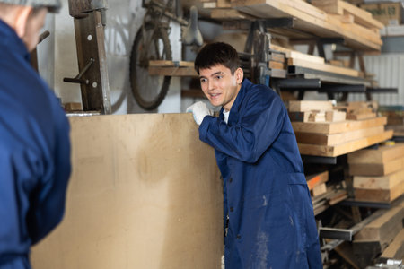 Young men carrying wooden board in workshop