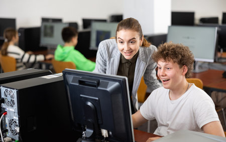Positive female teacher tells a teenager how to work on computer