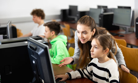 Female teacher talking to focused teen girl student in computer class
