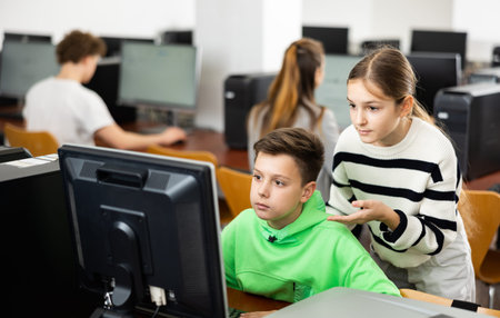 Schoolboy using computer at lesson, teacher teaching pupils in class room