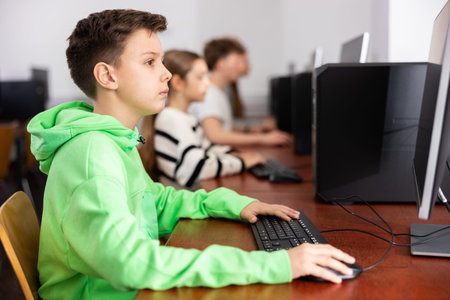 Schoolboy using computer at lesson, teacher teaching pupils in class room