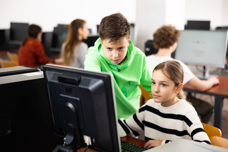 Teenage boy helping young girl with PC problem in computer class