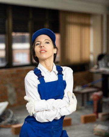 Positive woman repairer in uniform standing inside apartment and looking at camera