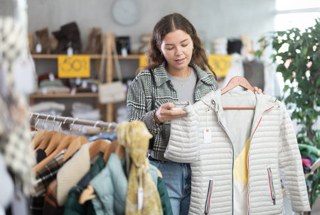 Young woman choosing down coat in clothing store