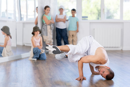 Experienced male trainer demonstrating to group of children dancers correct movements in hip-hop...