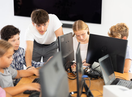 Guy teacher teaches boy student to work with computer