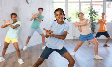 Positive juvenile boy engaged in Breakdancing in training room with childrens group