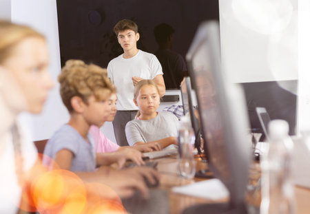 Guy teacher teaches group of students in computer class