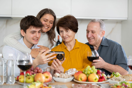 Senior woman and man celebrating family holiday with their son and his young wife at kitchen table,...