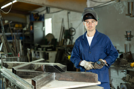 Male welder standing with a welding semi-automatic machine and a safety helmet in metal machining...