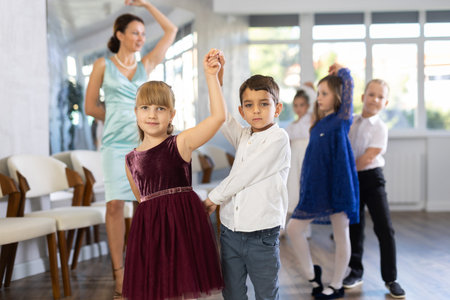 Little children in elegant dresses practicing waltz dance in school hall