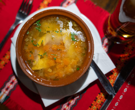 Deep clay bowl with Bulgarian fish and vegetable soup, complemented by cutlery and strong drinkの写真素材