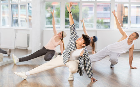 Man and his students perform hip hop dance on one bent leg, movement in horizontal plane near floor