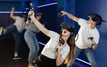 Young woman in VR glasses playing virtual game with handheld controllers