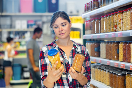 Young woman choosing preserved food in supermarketの写真素材