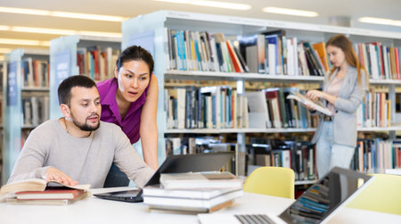 Woman and man looking at laptop screen together in library