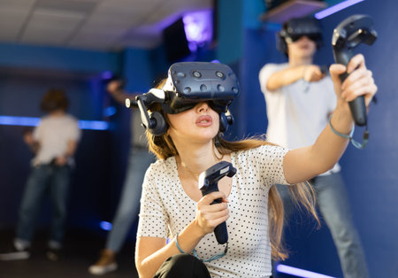 Young woman in VR glasses playing virtual game with handheld controllers
