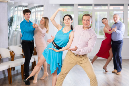 Positive men and woman dancing slow ballroom dance during group class in dance studio