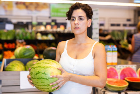 Latin american female shopper choosing ripe watermelon in supermarketの写真素材