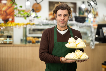 Positive cafe employee carries tray with fresh sweets