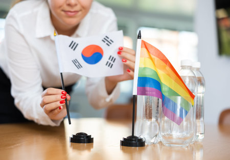 Young woman putting South Korea and LGBT flags on table in office
