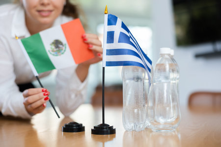 Unrecognizable girl sets midget flags of Greece and Mexico before international negotiations