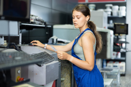Young woman worker operating computerised machine to mix paint in paint shop
