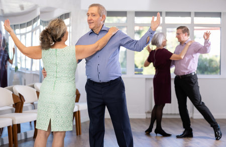 Smiling elderly woman and partner successfully perform mesmerizing movements of paso doble dance