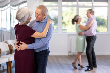 Elderly woman is dancing slow unhurried dance in hugs arms of her senior male partner.