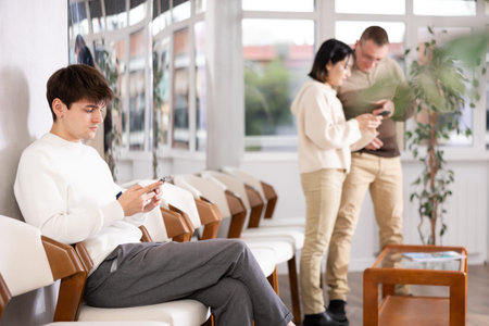Young guy sitting in line with phone