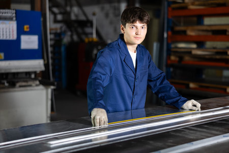 Guy working at metallurgical plant carefully measures sheet of iron using tape measure