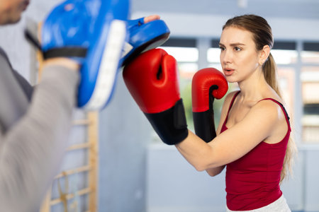 Athletic woman learns to box - hitting punch mitts. Woman with her trainer at gym