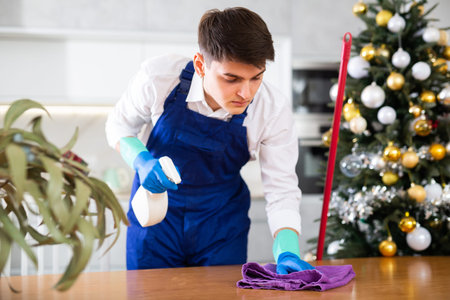 Man in uniform is ready to clean table in home before Christmas celebration