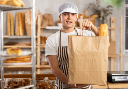 Dedicated young baker holding out bag of freshly baked goods