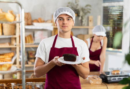 Young male seller with cake in bakery