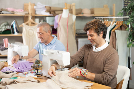 Two tailors sitting in a sewing workshop and working
