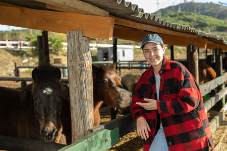 Portrait of smiling woman next to pony in stall at livestock farm