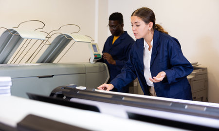 Attentiva woman working in publishing facility, loading large format paper in printer