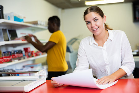 Attentive young female specialist verifying printed sheet during work in the print shop