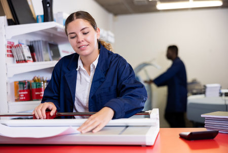 Work in printing house - woman cuts paper with professional cutterの写真素材