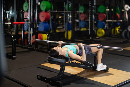 Woman performing bench chest press with barbell in gym