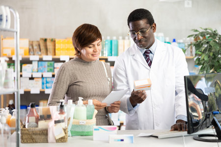 African man pharmacist uses computer at workplace and consulting woman clientの写真素材