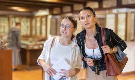 Young woman with teen daughter walk around museum, view antique appliances in museum hallの写真素材